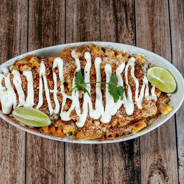 La Mesa Modern Mexican elote, a white bowl of corn with crema, chili powder, cheese, cilantro, and lime.
