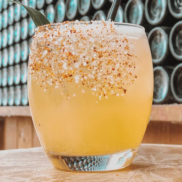 La Mesa Modern Mexican cocktail with a chili-salt rim and a pineapple leaf garnish.