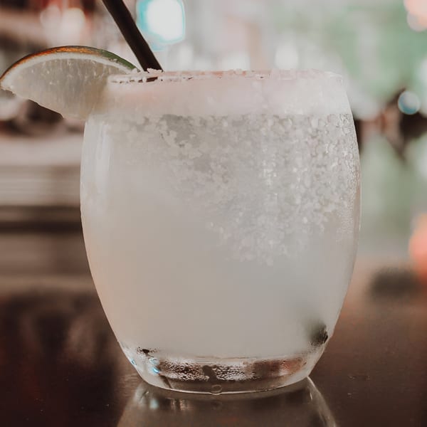 Close-up of a frosty margarita with a salted rim, lime wedge, and dark straw.