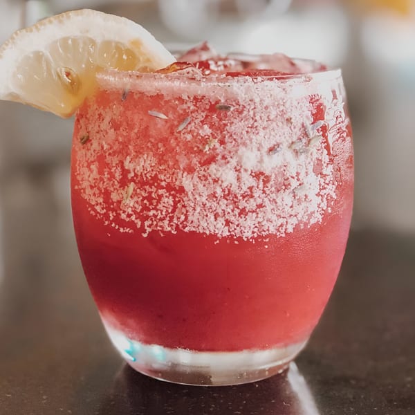 A vibrant red La Mesa Modern Mexican cocktail with a salted rim and lemon slice.