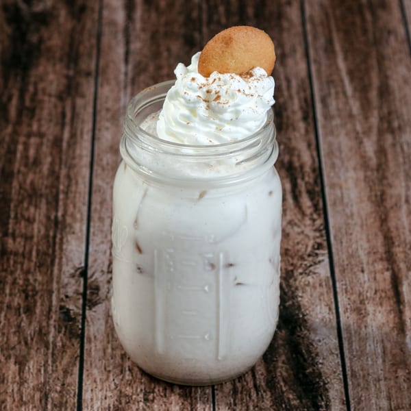 Horchata drink in a mason jar, topped with whipped cream, cinnamon, and a vanilla wafer.
