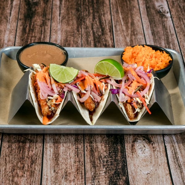Three La Mesa Modern Mexican tacos with fried fish, slaw, pickled onions, and lime on a tray.
